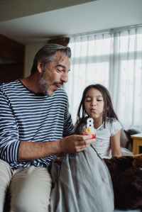 father and daughter blowing out a candle on a birthday cupcake